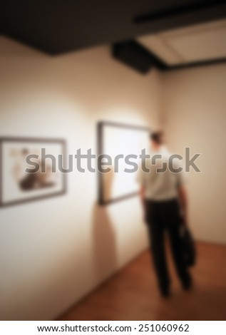 Man visits a photography gallery. Intentionally blurred editing post production. People, works and location not recognizable.