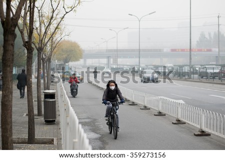 BEIJING, CHINA - NOVEMBER 14, 2015: An unidentified woman rides a bycicle during air pollution in Beijing. Air pollution is a serious problem in Beijing.