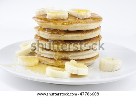 Pancakes or crepes on a white plate with honey and bananas on white background with short depth of field