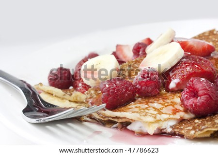 Pancakes or crepes on a white plate with honey and raspberries and strawberries on white background with short depth of field