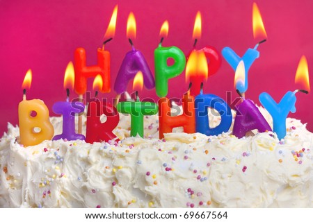 colourful lit candles spellign out happy birthday on a cake