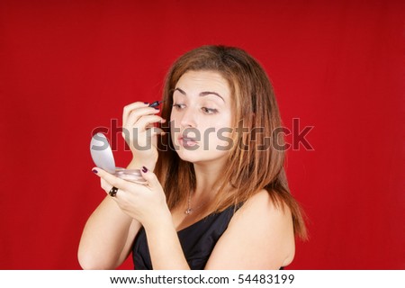 Portrait of a young woman applying liquid eye liner. Studio shot over red background.
