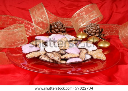 Gingerbread cookies in a red plate with gold candles, pine cones and Christmas ribbon. Studio shot over red background
