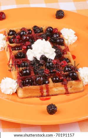 Waffle with soft fruits and whipped cream on an orange plate