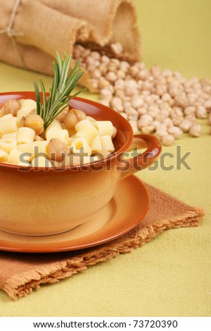 Small thimbles (ditalini) with chickpea and rosemary served in a ceramic bowl. Chickpeas spilling out from a jute bag in the background. Shallow DOF