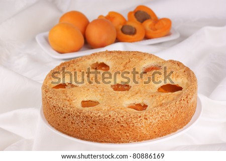 Apricot cake on a a white cake stand. Apricots out of focus in the background