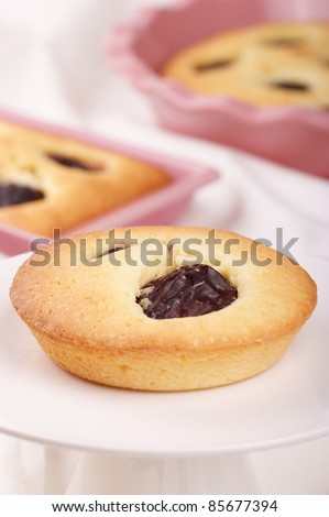 Small plum cake served on a white cake stand. Other plum cakes are out of focus in the background. Selective focus, shallow DOF.