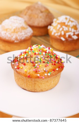 Muffin decorated with colored sugar grains on a cake stand and assorted muffins out of focus in the background. Selective focus, shallow DOF