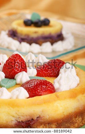 Strawberry cheese cake decorated with whipped cream and strawberries. Blueberry cheese cake out of focus in the background. Selective focus, shallow DOF