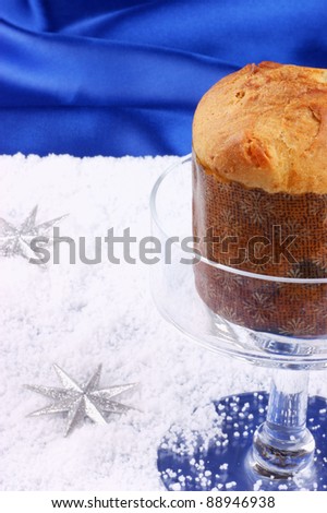 Christmas composition over a bright blue background: Panettone, a typical italian Christmas cake, served on a glass cake stand. Copy space. Selective focus, shallow DOF