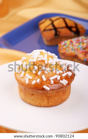 Muffin decorated with sugar grains on a cake stand and assorted muffins out of focus in the background. Selective focus, shallow DOF