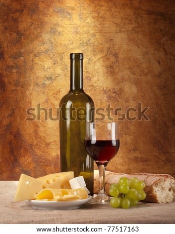 Red wine, assorted cheeses, bread and grapes in a still life setup.