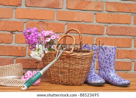 basket of flowers and gardening tools against a brick wall