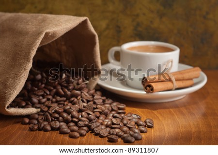 Coffee cup with burlap sack of roasted beans on rustic table . The sharpness of the coffee beans