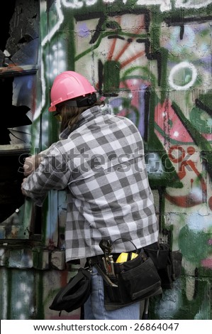 Worker taking out a window in a run down building with graffiti on it.