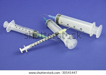 Four syringes on a blue background.They are all different sized syringes.