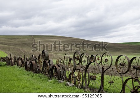 Old fence made of metal wheels.Rolling hill in background.