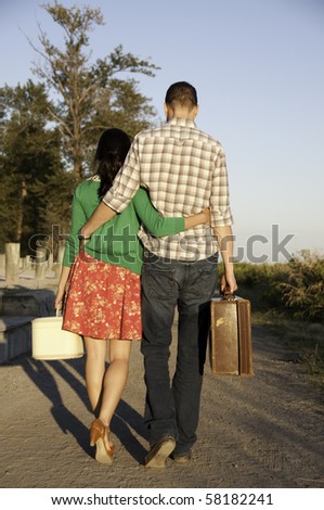 Young couple walking down path with their vintage suitcase in hand.They have arm around each other.
