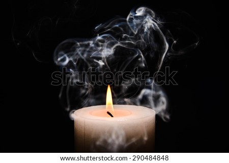 White burning candle with flame and smoke on black background.