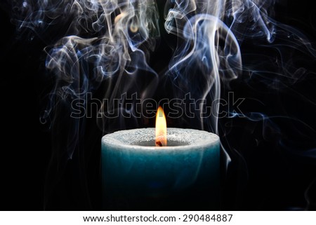 Light blue burning candle with flame and smoke on black background.