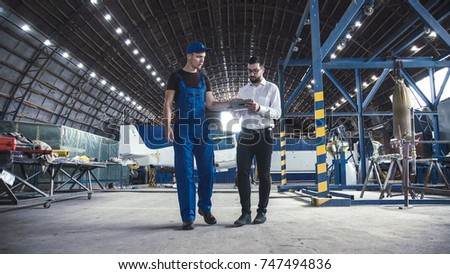 Mechanic and flight engineer having a discussion together as they stand in aircraft in a hangar.