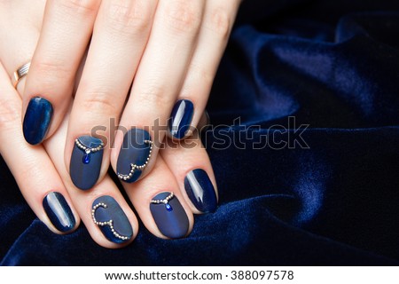 French manicure - beautiful manicured female hands with blue manicure with rhinestones on dark blue background