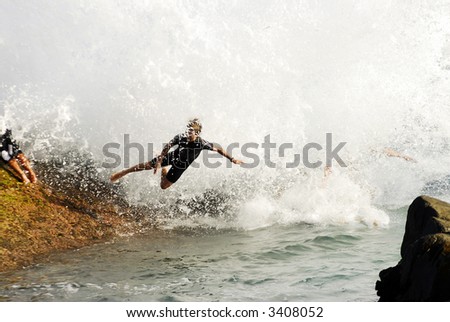 Young boy jumping off rock as wave crashes over