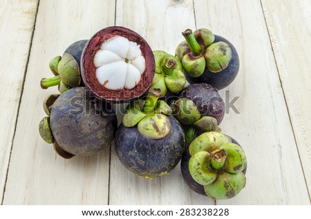 Mangosteen summer fruit cross section showing the thick purple skin and white flesh of the queen of fruits on wood background
