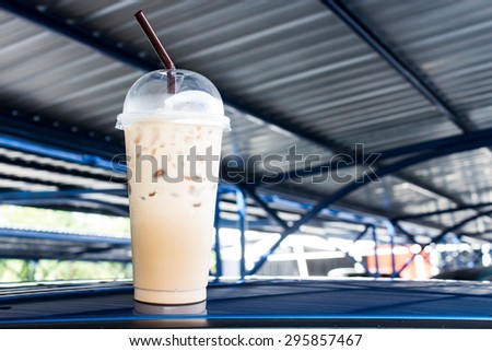 Iced coffee with straw in plastic cup on the top of car roof in the car park