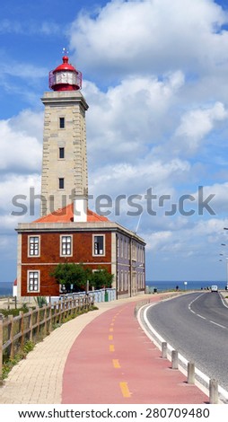 A road passes a lighthouse in the scenery of an amazing sky in Portugal.