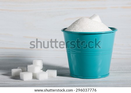 White sugar cubes and granulated sugar on white wooden background