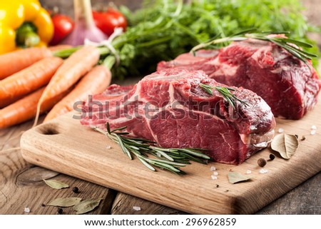Raw beef meat on cutting board and fresh vegetables on wooden table
