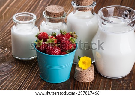 Milk in glass container and a bucket of strawberries on wooden table