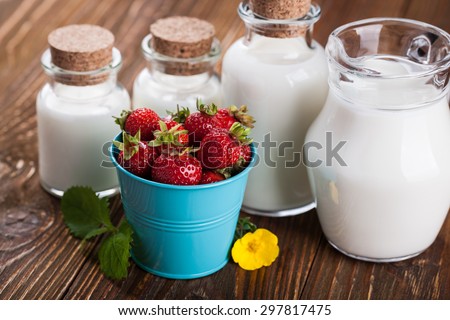Milk in glass container and a bucket of strawberries on wooden table