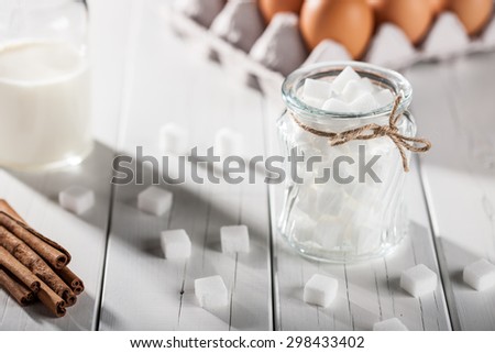 Eggs, milk, cinnamon, white sugar cubes on white wooden table