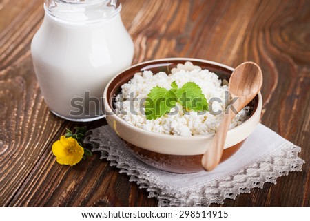 Bowl of cottage cheese and milk in glass pitcher on wooden table