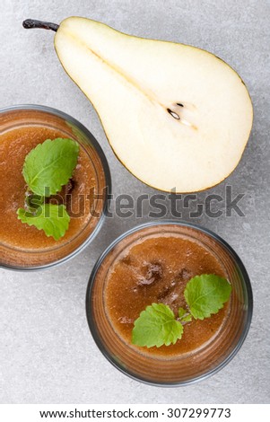 Two glasses of pear juices and ripe pear on the ceramic surface