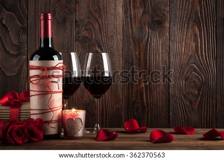 Red wine bottle, two glasses of wine, gift box, candle and red roses on the dark wooden background