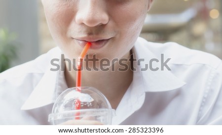 Asian young man using a straw to drink from a plastic cup.