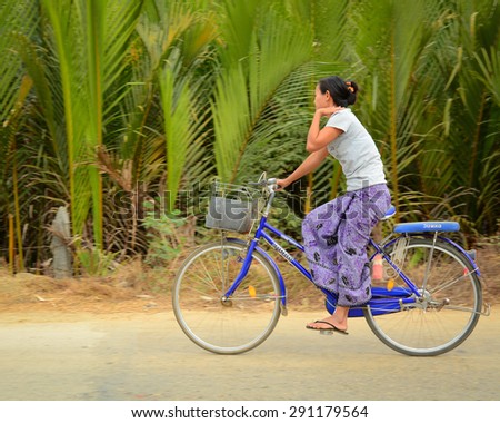 Ngapali, Myanmar - Jan 22, 2015. Burmese woman rides bicycle along countryside street in Ngapali, Myanmar.