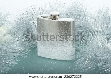 Frozen brushed metal flask on ice with snow and Christmas garland on background