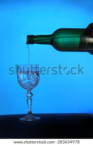 A blue back lit image of wine being poured from a bottle into a diamond cut glass