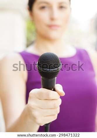 Female holding microphone to viewer. Focus is on microphone.
