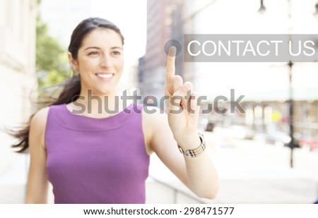 A smiling young woman on a city street presses a virtual CONTACT US button.