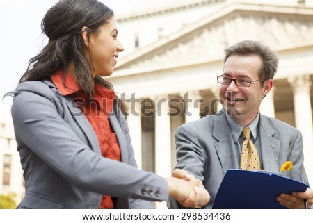 A man holding a clipboard shakes the hand of a woman. The man could be interviewing or conducting a survey.