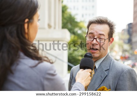 A smiling well dressed man being interviewed by a woman with a microphone. Focus is on man\'s face.