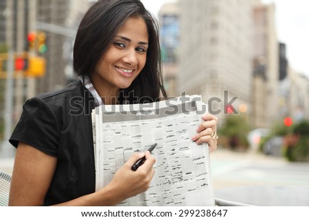 A smiling woman holding up a newspaper pointing to job listings. Focus is on her face.