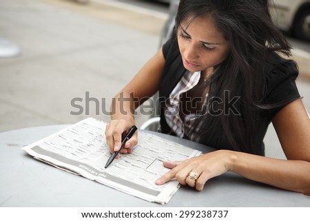 A seated woman looking the the job listings in a newspaper. Focus is on her face.