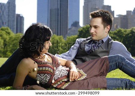 A young couple in the park lying on sides look at each other. Focus on woman.
