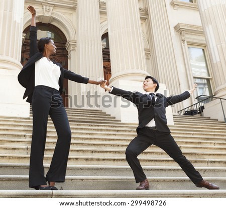 A man and woman dressed as legal/business professionals, dancing on the steps of a building celebrating success.